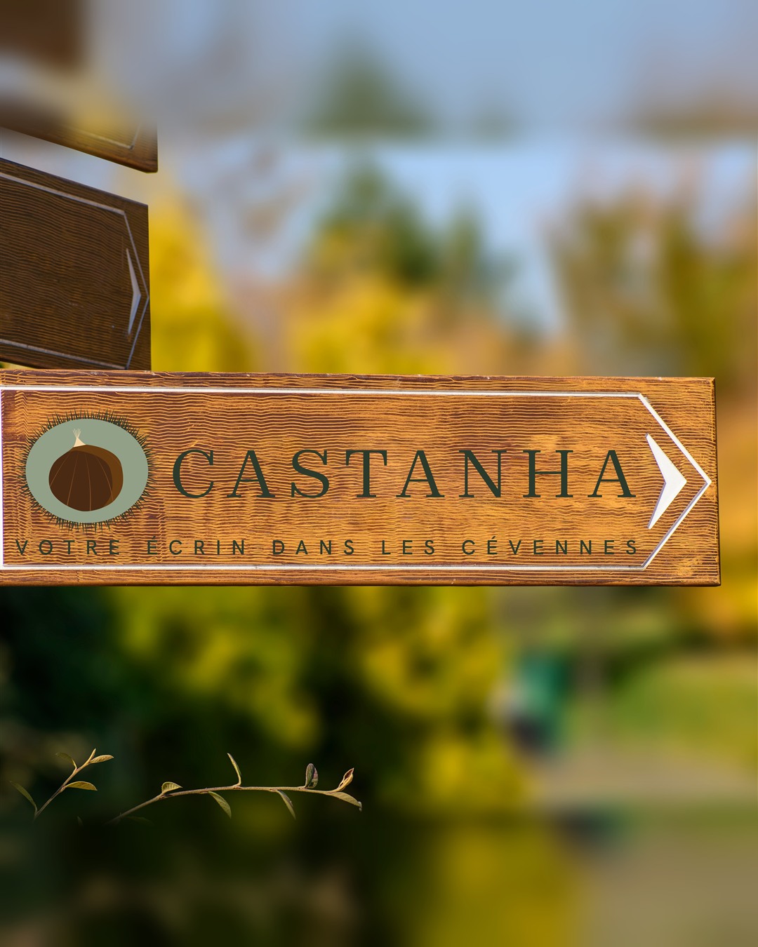 Le logo Castanha sur un panneau directionnel en bois, à l'entrée du chemin